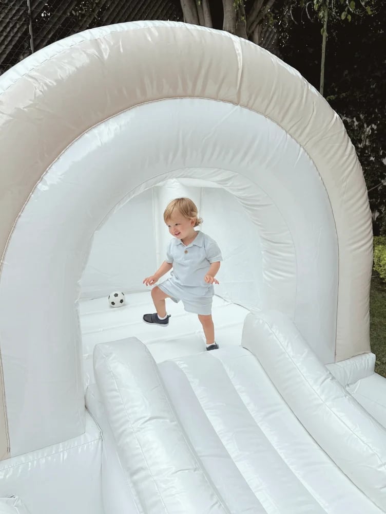 Toddler playing inside a white inflatable bounce house tunnel with a small soccer ball