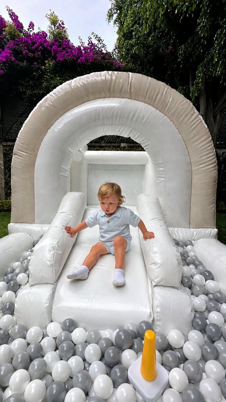 Toddler sliding down a white inflatable bounce house slide filled with gray and white plastic balls