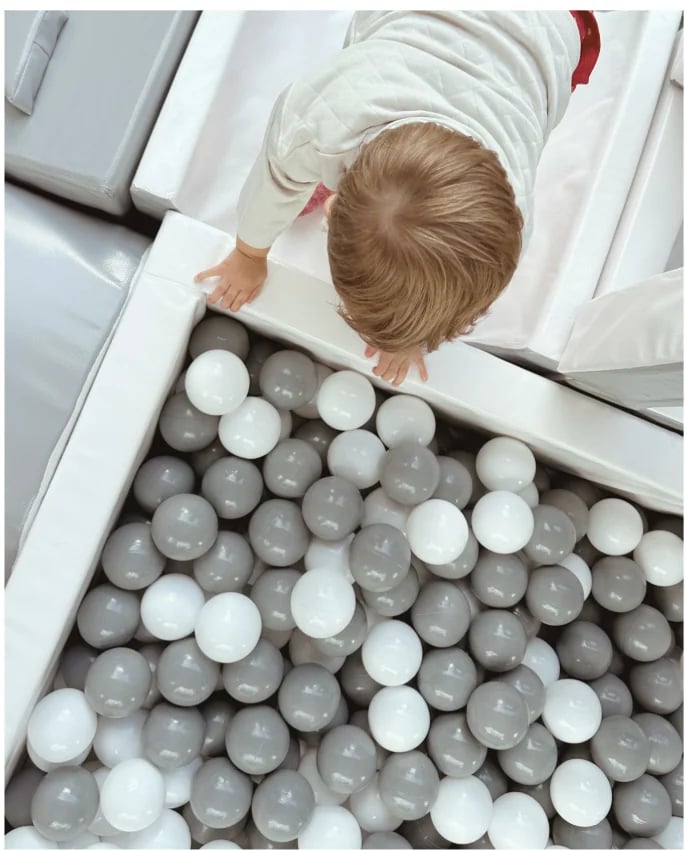 Overhead view of a toddler in a white shirt playing in a ball pit filled with gray and white plastic balls