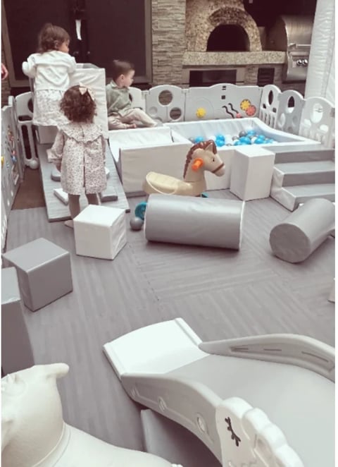 Toddlers playing in a modern white modular play structure with soft foam elements, balls, and toys in an indoor playroom
