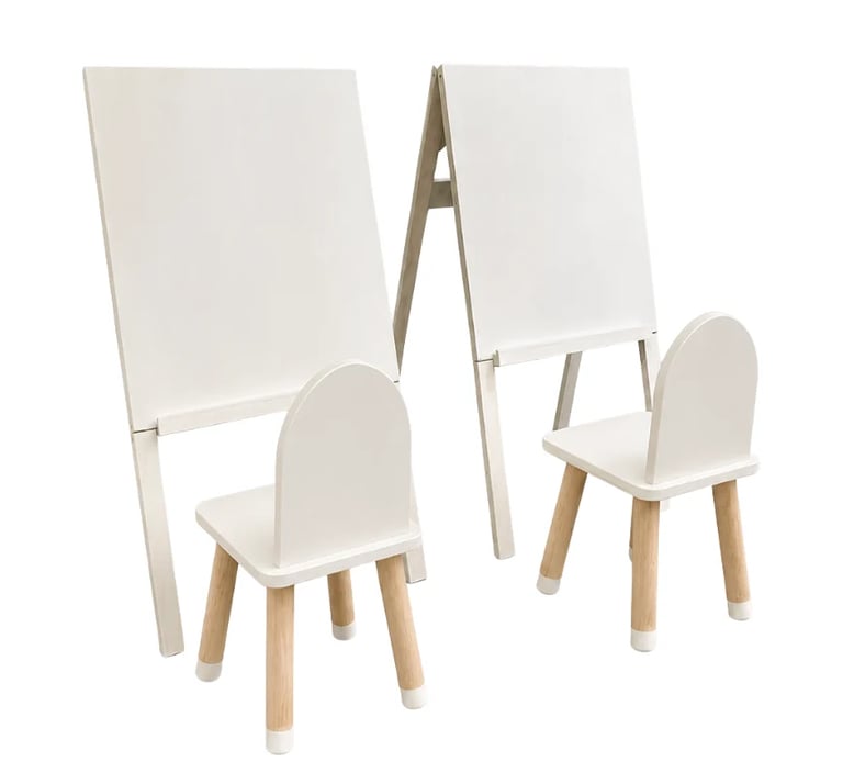 Two white childrens easels with attached chairs and wooden legs, featuring blank drawing boards