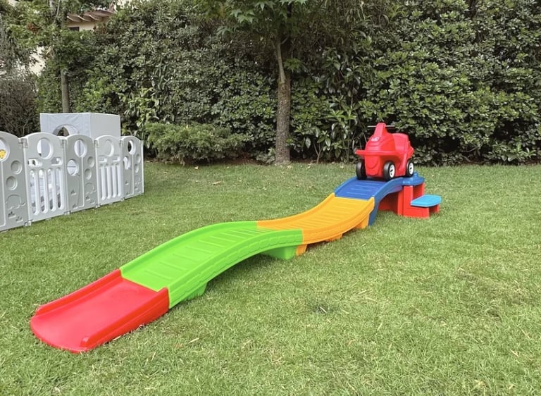 Colorful childrens slide with red and green sections in a grassy backyard with decorative gate and trees