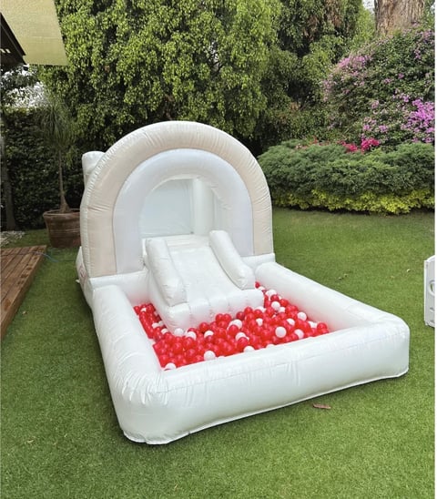White inflatable bounce house with slide and ball pit filled with red and white balls on grass lawn